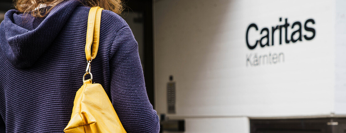 Person mit gelber Tasche steht vor Eingang der Caritas Kärnten und sucht Unterstützung.