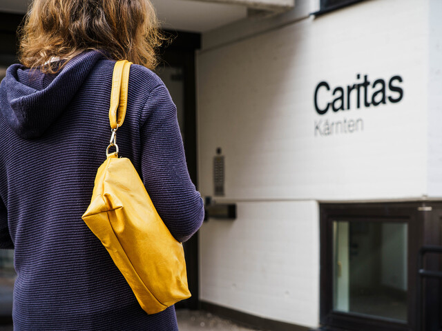 Person mit gelber Tasche steht vor Eingang der Caritas Kärnten und sucht Unterstützung.