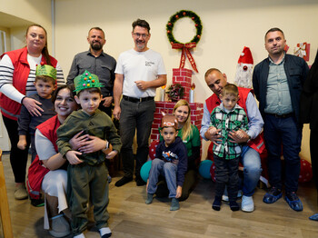 Gruppe von Erwachsenen und Kindern bei einer weihnachtlichen Hilfsaktion mit Deko, Geschenken und Nikolausfigur.
