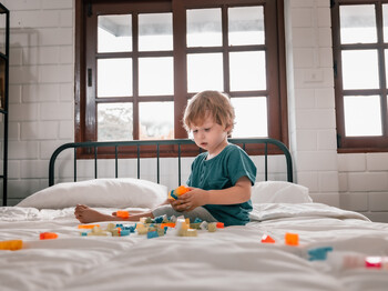 Ein Kind sitzt mit Spielzeug auf einem Bett.