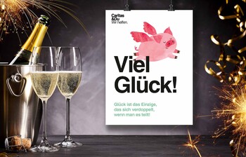 Ein Sektkübel, mit Sekt und gefüllte Sektgläser stehen auf einem Tisch, als Symbol für Silvester und das neue Jahr. Daneben hängt ein Plakat mit einem fliegenden Schwein auf dem "Viel Glück" steht.