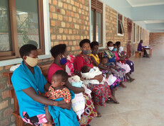 Mütter mit ihren Kindern sitzen an Bänken auf der Wand und warten.