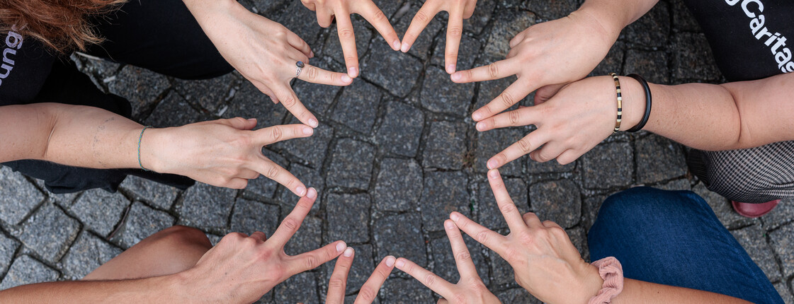 Personen sitzen im Kreis zusammen und formen mit ihren Fingern einen Stern, der Zusammenhalt symbolisiert.