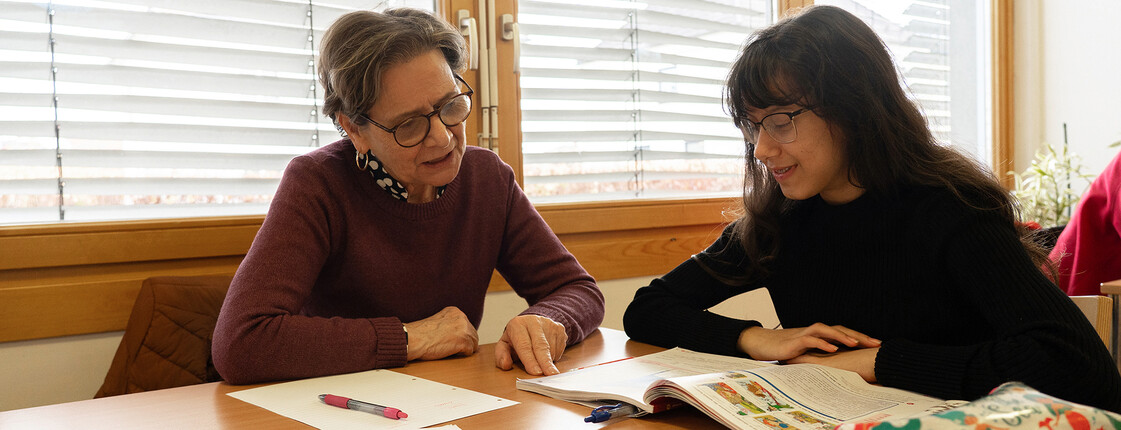 Zwei Personen sitzen am Tisch und arbeiten gemeinsam mit Schulbüchern und Lernunterlagen.