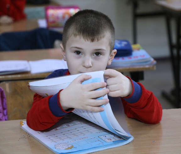 Aldin, ein Junge mit Behinderung, öffnet sein Schulbuch in seinem Klassenzimmer.