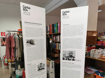 Zwei große weiße Säulen mit den wichtigsten Informationen zu 100 Jahre Caritas stehen im Second-Hand-Markt carla.