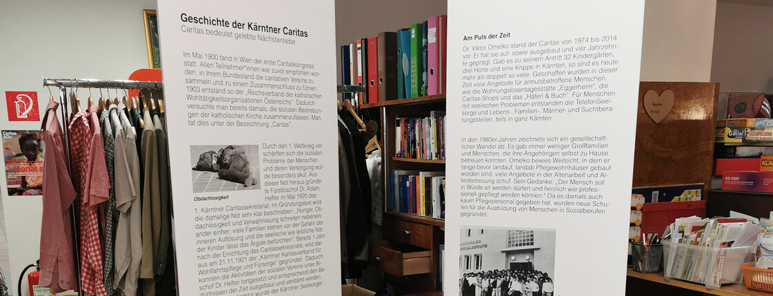 Zwei große weiße Säulen mit den wichtigsten Informationen zu 100 Jahre Caritas stehen im Second-Hand-Markt carla.