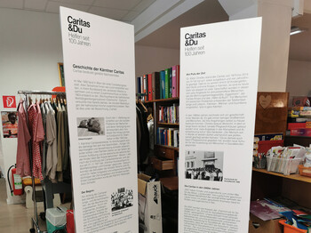 Zwei große weiße Säulen mit den wichtigsten Informationen zu 100 Jahre Caritas stehen im Second-Hand-Markt carla.
