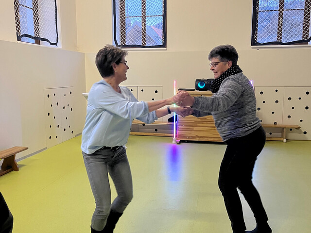 Zwei Damen halten sich an den Händen und tanzen in einem Turnsaal.