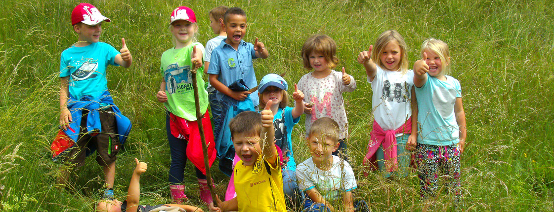 Kinder des Kindergarten Kunterbunt in Deutsch-Griffen stehen auf einer blühenden Wiese und lächeln in die Kamera.