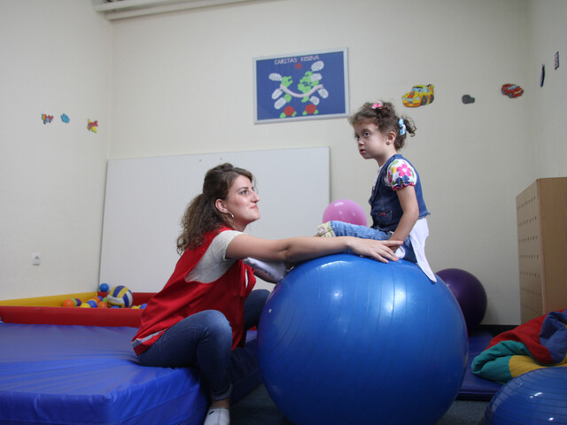Eine Betreuerin hilft einem Mädchen mit dem Gleichgewicht, während es auf einem Gymnastikball sitzt