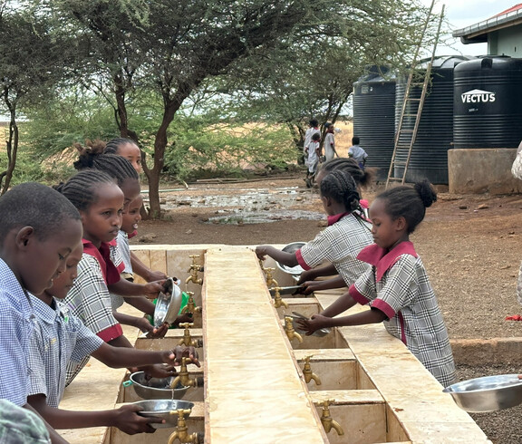 Schüler*innen spülenin spült Essgeschirr im Freien an der Tiigo School in Kenia