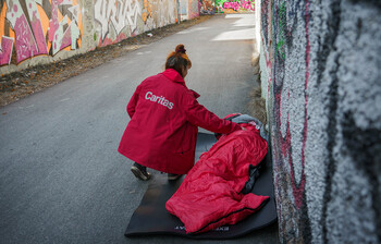 Eine Caritas-Mitarbeiterin bringt einem obdachlosen Menschen einen Schlafsack – praktische Hilfe für Menschen ohne Dach über dem Kopf.