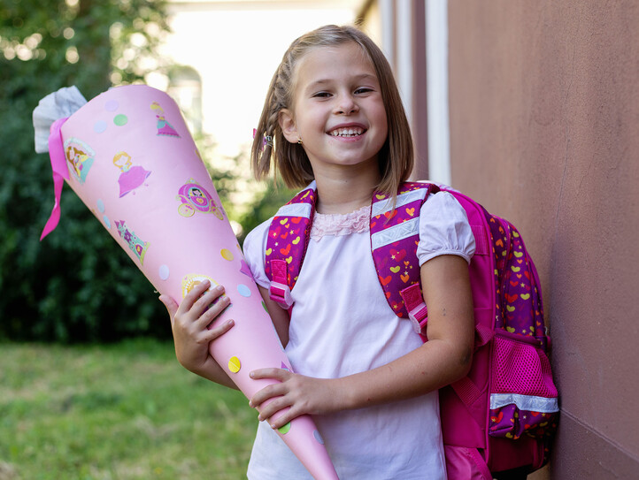 Little kid girl with school satchel on first day to school, holding school cone with gifts