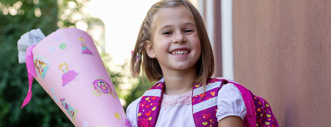 Little kid girl with school satchel on first day to school, holding school cone with gifts Ein Mädchen hält eine rosa Schultüte in der Hand und trägt einen pinken Rucksack.