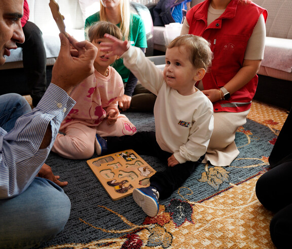 Kind hebt ein Puzzleteil hoch, während andere Teile auf dem Teppich liegen