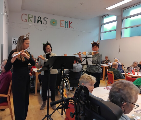 Drei Musiker*innen mit Flöten musizieren vor Bewohner*innen im festlich geschmückten Raum