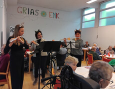 Drei Musiker*innen mit Flöten musizieren vor Bewohner*innen im festlich geschmückten Raum