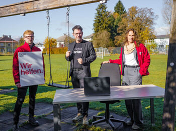 Drei Caritas-Mitarbeitende mit Tisch und Plakat am Spielplatz als Zeichen gegen Care-Arbeits-Überlastung.
