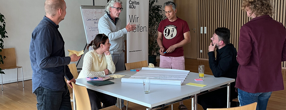 Teilnehmende diskutieren beim Caring Community Netzwerktreffen der RegionalCaritas St. Veit an einem Arbeitstisch.