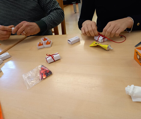 Menschen aus unserem Projekte rollen Sprüche auf Papier zusammen und verpacken diese mit einer Schleife.