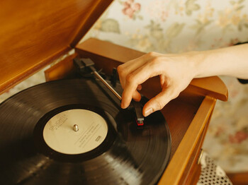 Hand legt Nadel auf Schallplatte  Hand legt Tonarm auf schwarze Vinylplatte mit Oldies der 60er bis 80er in Holzplattenspieler