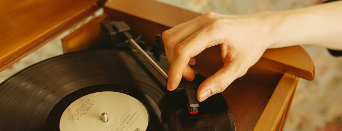 Hand legt Tonarm auf schwarze Vinylplatte mit Oldies der 60er bis 80er in Holzplattenspieler