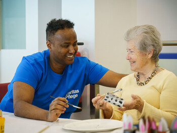 Pflegekraft unterstützt ältere Bewohner*in bei kreativer Beschäftigung im Pflegewohnhaus Haus Suavitas von Caritas.