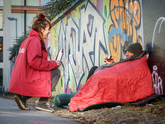 Eine Caritas-Mitarbeiterin bringt einem obdachlosen Mann warmen Tee – Hilfe und Menschlichkeit direkt auf der Straße.