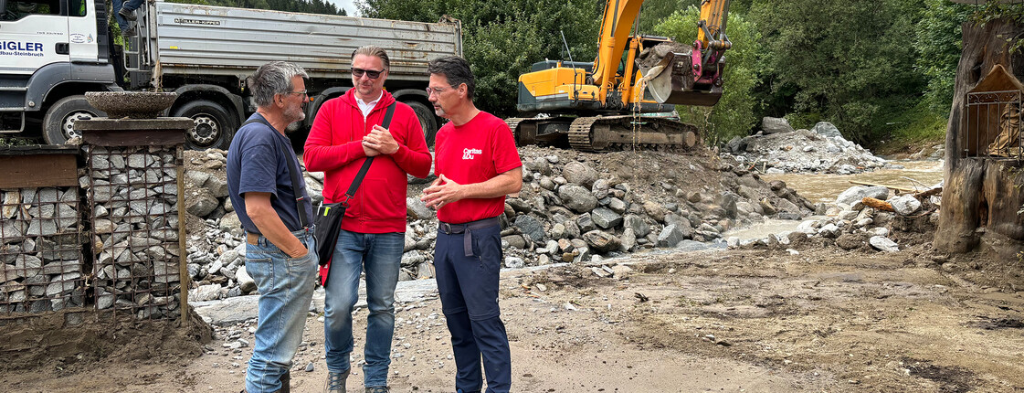 Caritas Direktor Ernst Sandriesser und Katastrophenleiter Christian Eile unterhalten sich mit einem Betroffenen in einem Überschwemmungsgebiet.