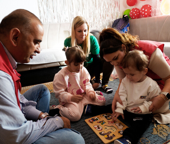 Zwei Kinder setzen Holzpuzzleteile ein, umgeben von Betreuungspersonen