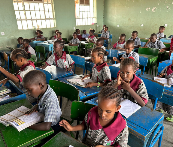 Kinder sitzen in einem einfachen Klassenzimmer der Tiigo School und verfolgen den Unterricht.