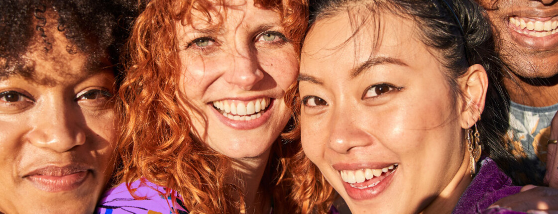 Eine Gruppe von vier Menschen die eng aneinander stehen und lächeln.