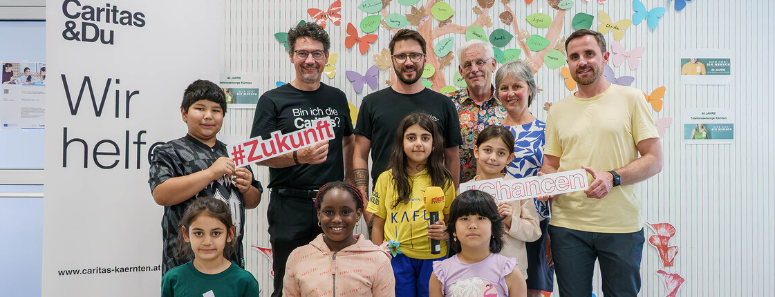 Gruppe aus Kindern und Erwachsenen im Lerncafé mit Schildern zu #Zukunft und #Chancen bei der Antenne-Schulstartaktion.