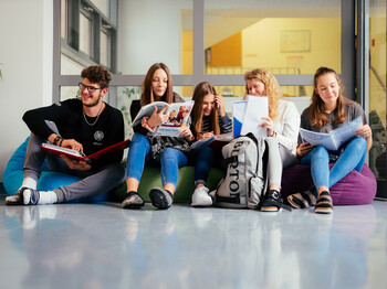 Ein Schüler und fünf Schüler*innen sitzen auf Sitzsäcken im Gand der Schule und lernen miteinander.