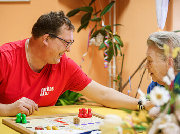 Freiwilliger aus dem Caritas: Team Lebensgstaltung spielt mit einer Bewohnerin im St. Hemma-Haus ein Brettspiel.
