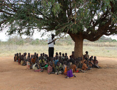 Im Schatten eines Baumes in Uganda werden viele Kinder von einem Lehrer unterrichtet.