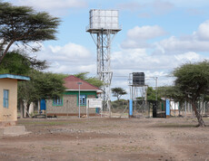 Wasseranlage mit hohem Tankturm, Gebäuden und Zaun in trockener Landschaft zur Trinkwasserversorgung.