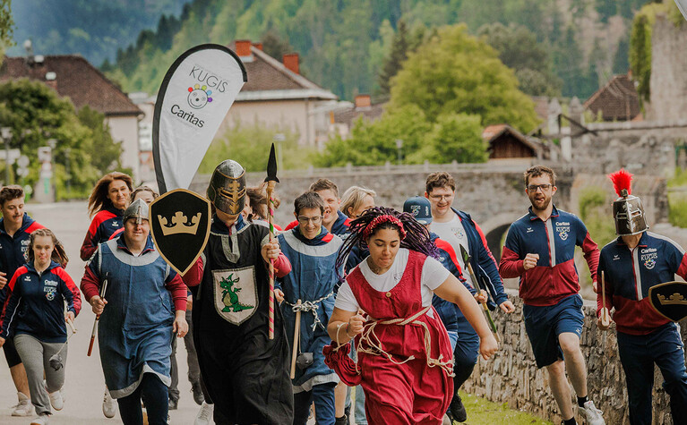 Ritter und Läufer nehmen an einem Event teil, ein Banner mit Caritas KUGIS ist zu sehen.