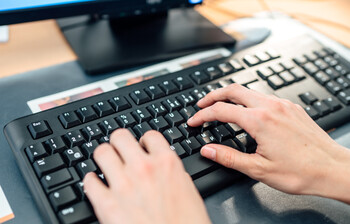 Frauenhände tippen etwas auf einer Computer-Tastatur ein.