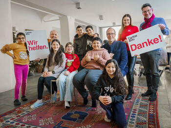 Gruppe im Lerncafé mit Schildern „Wir helfen.“ und „Danke!“ bei Spendenübergabe