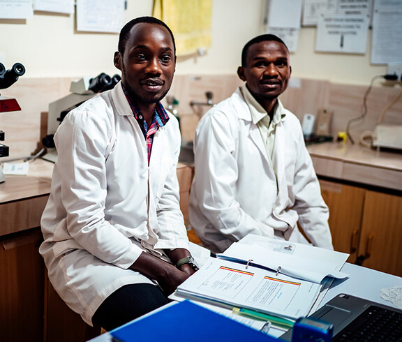 Zwei Ärzte sitzen im Büro vor Unterlagen und lächeln.