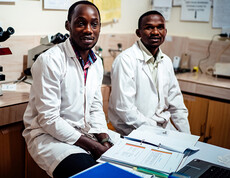 Zwei Ärzte sitzen im Büro vor Unterlagen und lächeln.
