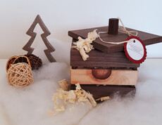 Eine braune Holzbox mit Zirbenspännen gefüllt auf Watte und vor einem weißen Hintergrund drapiert.