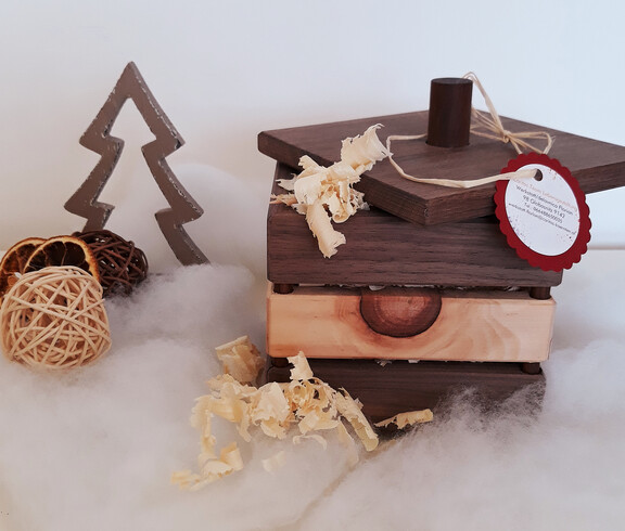 Eine braune Holzbox mit Zirbenspännen gefüllt auf Watte und vor einem weißen Hintergrund drapiert.