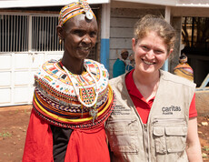 Caritas-Projektreferentin Theresa Sacher steht gemeinsam mit einer afrikanischen Frau in Marsabit. Beide lächeln, im Hintergrund sind weitere Personen und Gebäude zu sehen. Die Szene zeigt den direkten Austausch bei einem Projektbesuch.