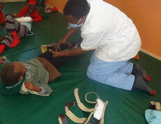 Ein Mädchen liegt auf einer Matte. Ein Pfleger hilft ihr bei medizinischen physiotherapeutischen Übungen.