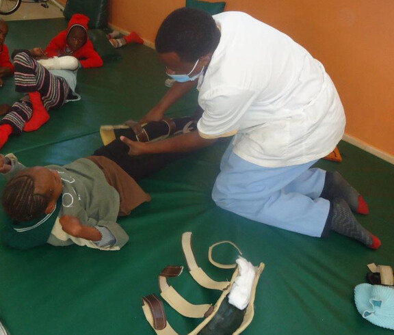 Ein Mädchen liegt auf einer Matte. Ein Pfleger hilft ihr bei medizinischen physiotherapeutischen Übungen.