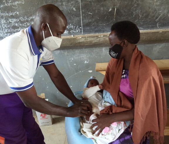 Eine Mutter hält ihr Baby im Arm, während ein Arzt das Kind impft.