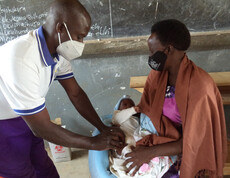 Eine Mutter hält ihr Baby im Arm, während ein Arzt das Kind impft.